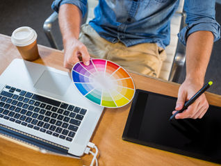 Designer selecting colors using a color wheel while working on a laptop and digital tablet, illustrating the role of color psychology in digital marketing and branding decisions