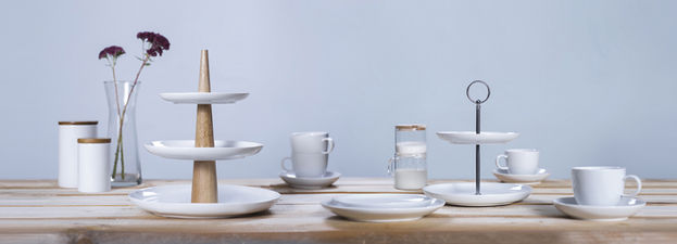 Produktfotografie von weißem Geschirr, Tassen und Tableware auf einem Holztisch, dekoriert mit Blumen und weiteren Wohnaccessoires.