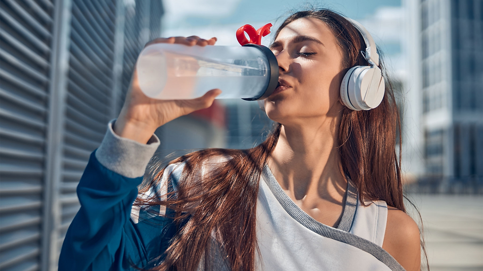 Woman in headphones drinks from a water bottle outdoors. She's wearing a blue jacket, with a red bow in her hair, enjoying a sunny day.