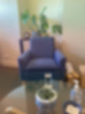 A counseling room with a comfortable blue armchair, potted plants, a glass of water, a box of tissues and LGBT+ affirming pins.