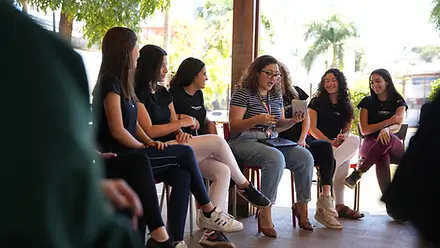 Estudantes sentados em roda em área externa, conversando com uma orientadora