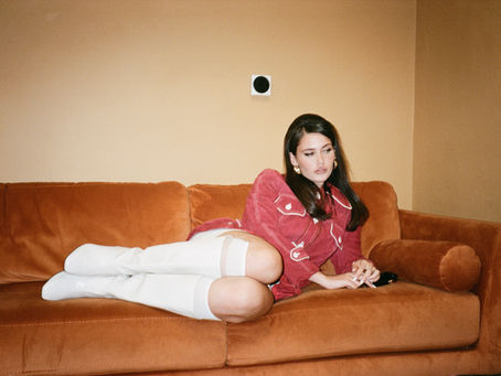 Sienna Spiro sitting on a couch wearing white boots.