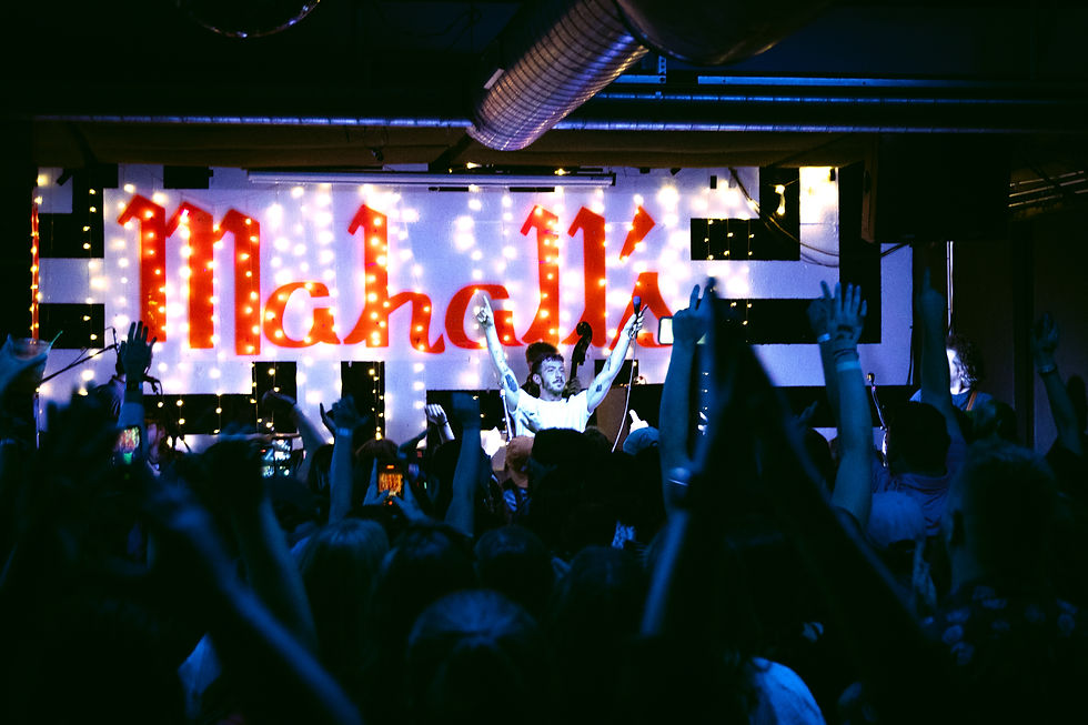 Crowd cheers as a singer raises both arms on a lit stage with a glowing Mikhail sign.
