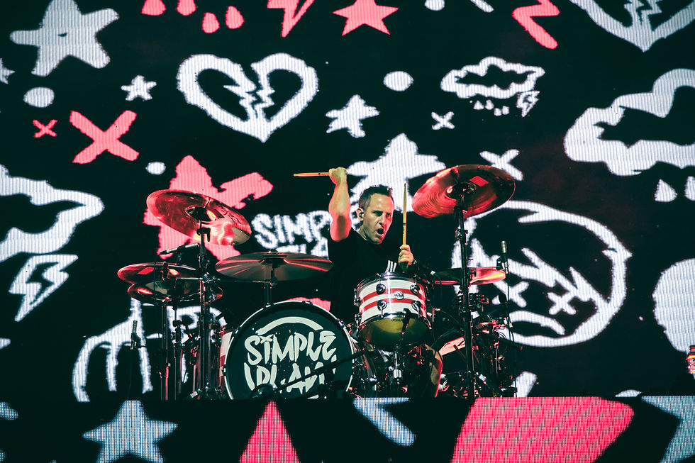 Drummer on stage playing under a red-and-white graffiti backdrop, with Simple Plan on the bass drum and an intense concert mood.