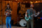 The Drive Home sings and plays guitar and bass in a garage band setup under string lights, with THE DRIVE HOME banner.