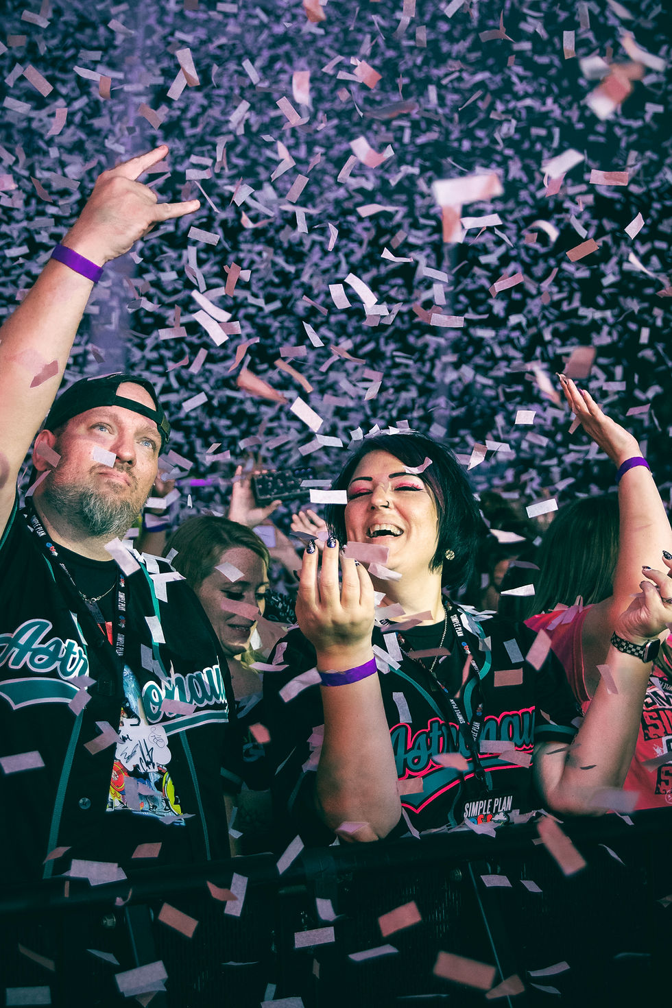 Confetti rains over smiling concert fans in Simple Plan shirts, hands raised in a joyful crowd.