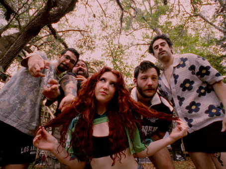 Five friends lean toward a low camera under tree branches, with a red-haired woman centered and a pink sky overhead.