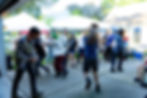 People dancing and chatting at a backyard party under white tents, with drinks and lawn chairs in bright afternoon light.