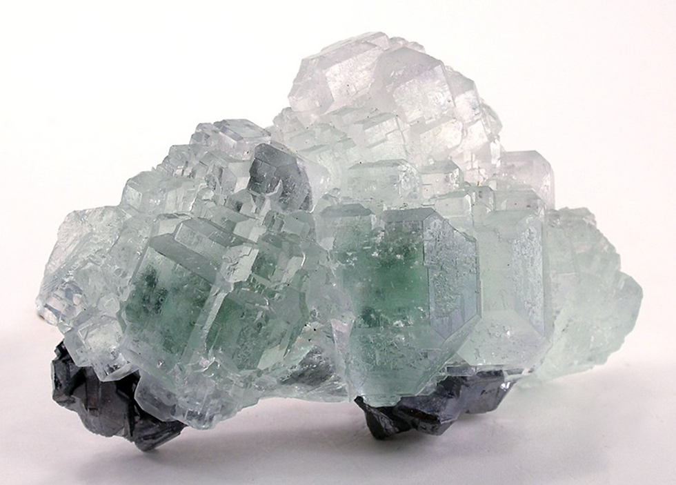 Translucent pale blue and green mineral crystals with cube-like formations on a white background. The texture appears rough and jagged.