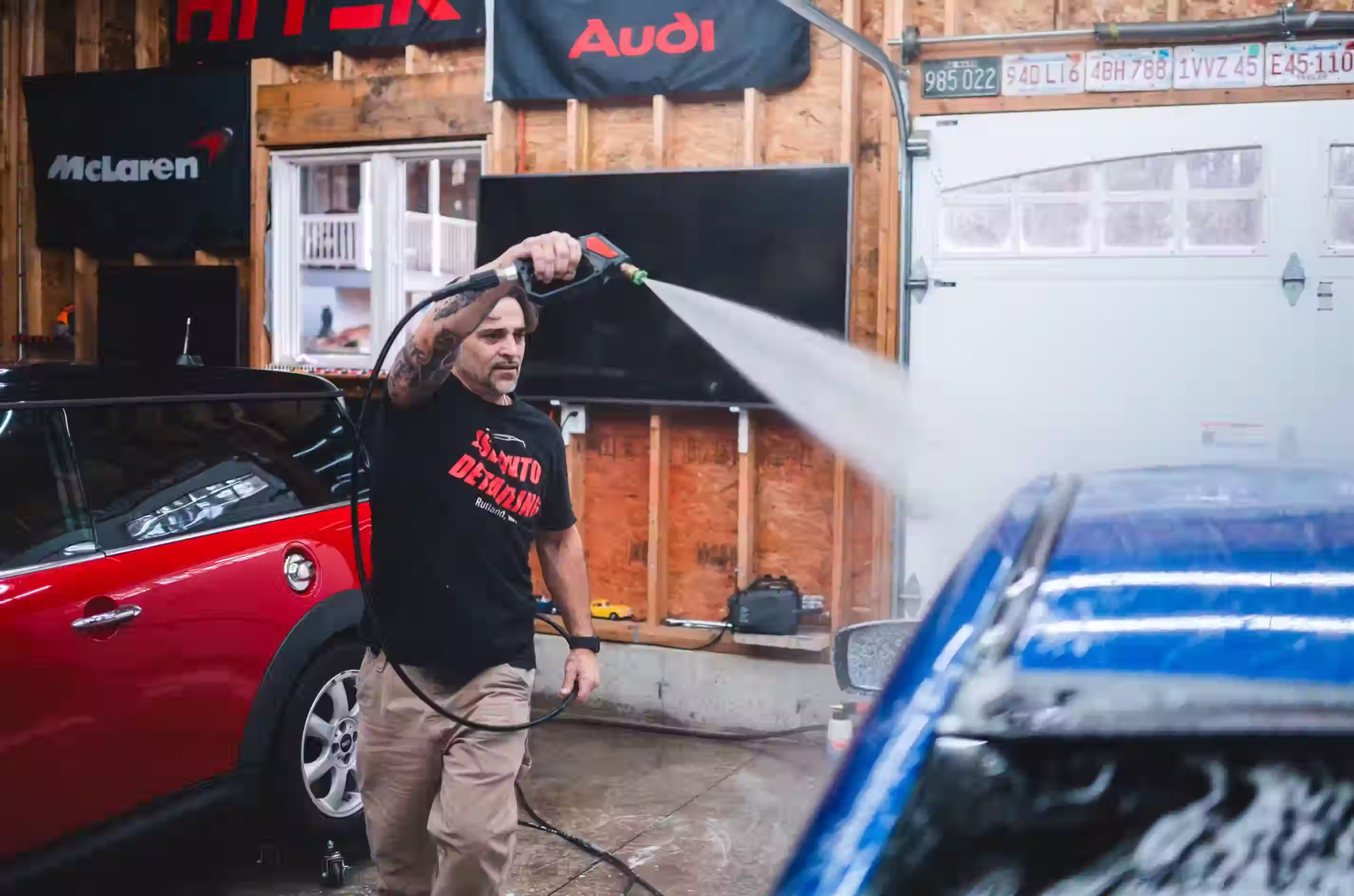 Jason pressure-washing a red car outside the shop