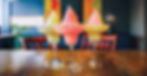 Three colorful soft serve margaritas in glasses, sitting on a wooden table in a vibrant setting with art in the background.