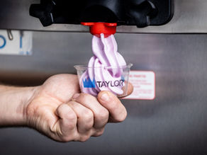 hand holding soft serve in a cup as its being dispensed from a soft serve machine