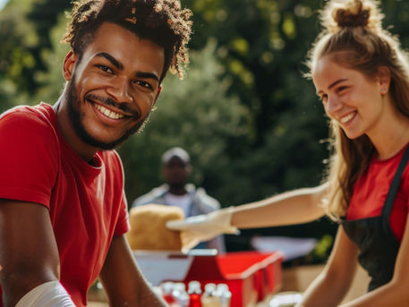 Volunteers in red shirts smiling and working together during a community service activity outdoors.