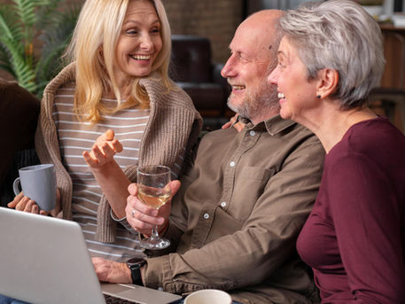Friends gathered on a couch smiling and laughing while watching a video together, celebrating a 60th birthday.
