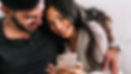 Couple smiling while looking at a phone together, reacting to an anniversary message.