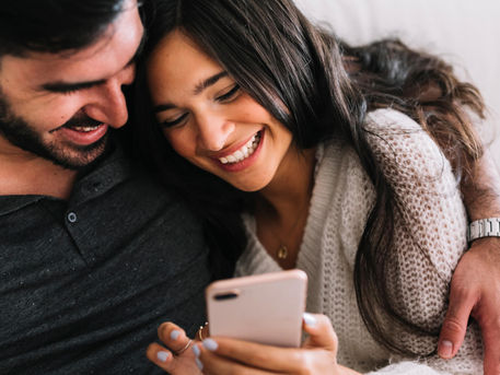 Couple smiling while looking at a phone together, reacting to an anniversary message