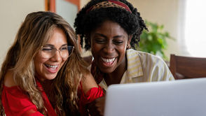 Two friends laughing while watching a birthday video message on a laptop