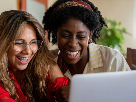 Two friends laughing while watching a birthday video message on a laptop