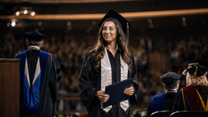 Graduate in cap and gown holding a diploma cover after walking across the commencement stage during a graduation ceremony.
