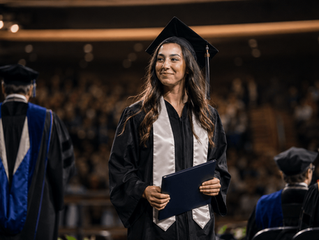 Graduate in cap and gown holding a diploma cover after walking across the commencement stage during a graduation ceremony.