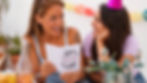 Woman smiling while reading a short birthday wish in a birthday card with a friend beside her.