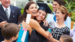 Graduate in cap and gown hugging a family member while surrounded by smiling relatives during a graduation celebration outdoors.