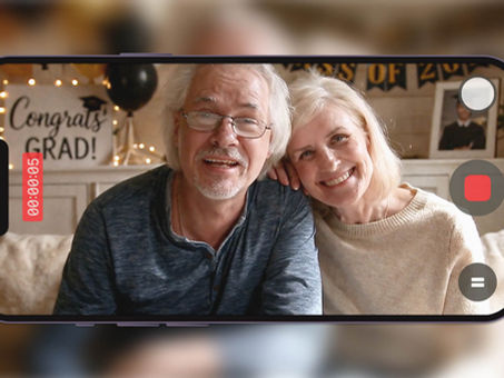 Parents smiling and recording a graduation video message with “Congrats Grad” decor behind them.