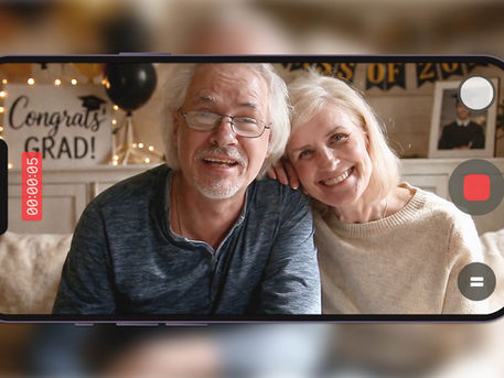 Parents smiling and recording a graduation video message with “Congrats Grad” decor behind them.