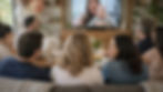Friends and family gathered in a living room watching a personalized video gift on TV.