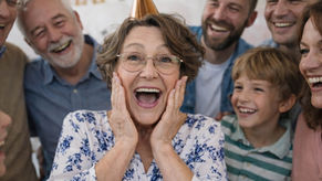 Woman reacting with surprise and joy to a 60th birthday gift, surrounded by family celebrating together.