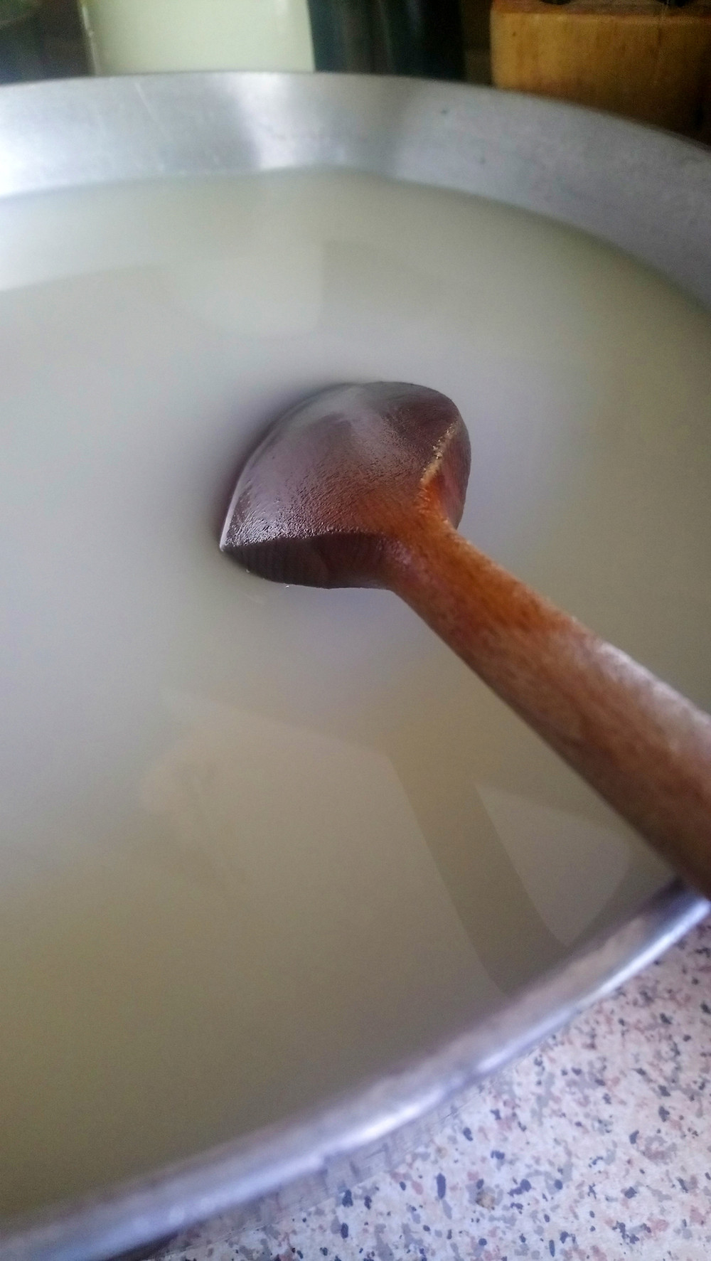 a wooden spoon sitting in an aluminium pot full of soya milk and water
