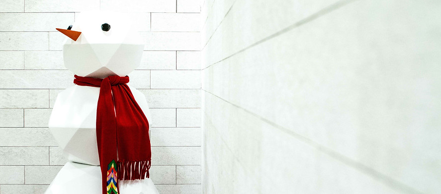 Very sharply structured snowman, appears to be made out of paper, wearing a red scarf, in front of a white brick background