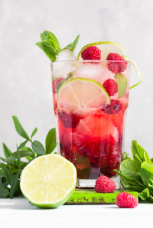 Lemonade or non-alcohol cocktail with raspberry, lime and mint in glass on grey background
