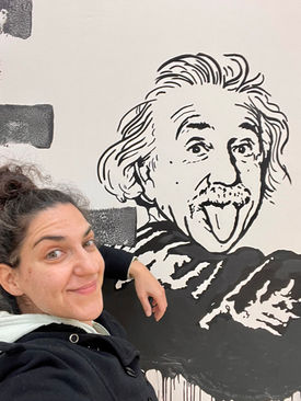 An artist posing beside her black-and-white mural of Albert Einstein sticking out his tongue