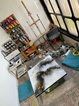 Artist's cluttered studio with an unfinished abstract painting on the table and art supplies scattered around