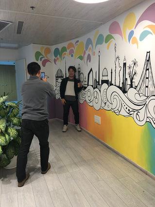 Two people posing in front of a vibrant mural featuring global landmarks and colorful waves