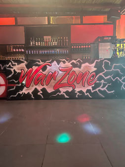 Bar counter with a 'War Zone' graffiti mural under colorful lights