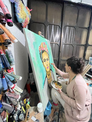 Artist painting a portrait of Frida Kahlo on a large canvas in her studio, surrounded by art supplies