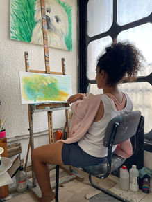 Art student as part of a art workshop  working on a watercolor painting of a landscape, with a dog painting on the wall above her.