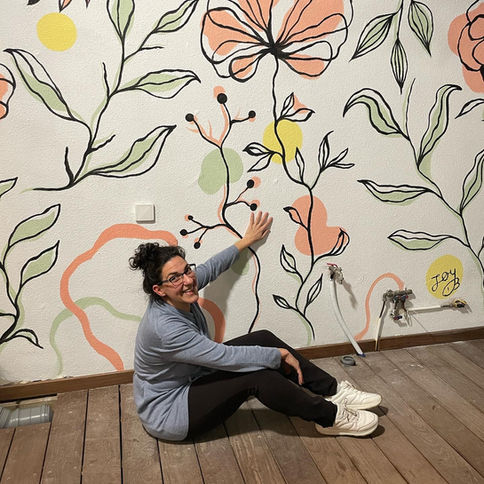 A vibrant hand-painted mural with abstract floral designs in soft colors of orange, green, and yellow, on a white wall."
