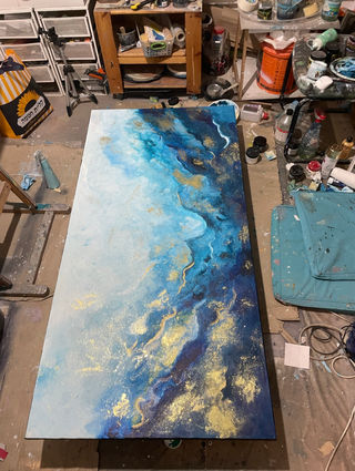 Abstract painting with blue, teal, and gold swirls on a canvas in an artist's studio