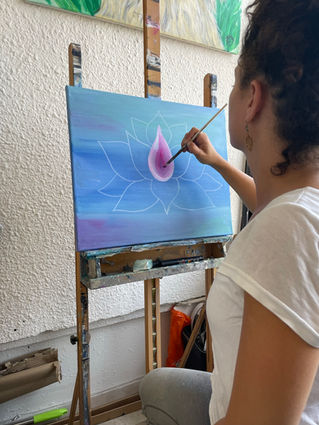 Artist painting a pink lotus flower on a blue background in her studio