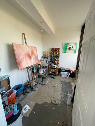 Artist's workspace with a large canvas on an easel, art supplies scattered around, and a painting of a dog on the wall