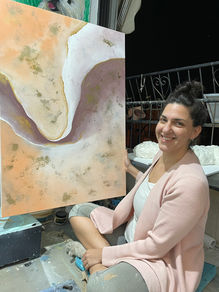 Artist sitting on the floor, smiling while holding her abstract painting featuring soft earthy tones