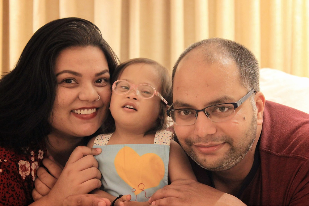 Indian Man and Woman smiling at their camera with their daughter who has Downs Syndrome