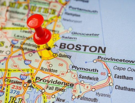 Paper map showing the eastern side of Massachusetts with a red pin set on Boston, MA.