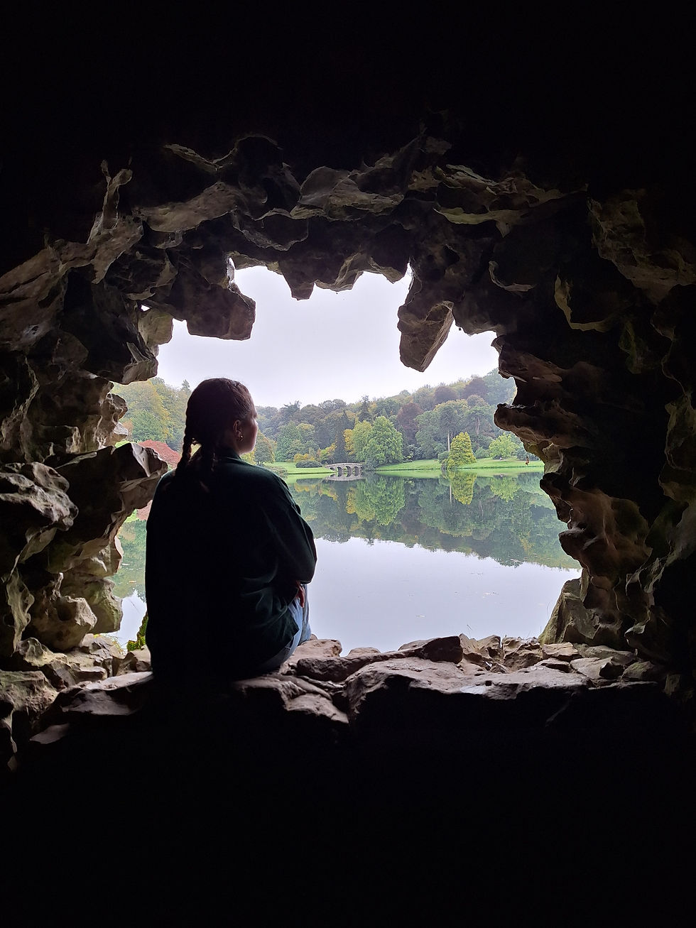 Alice stares through a gap in the rock wall onto a lake beyond