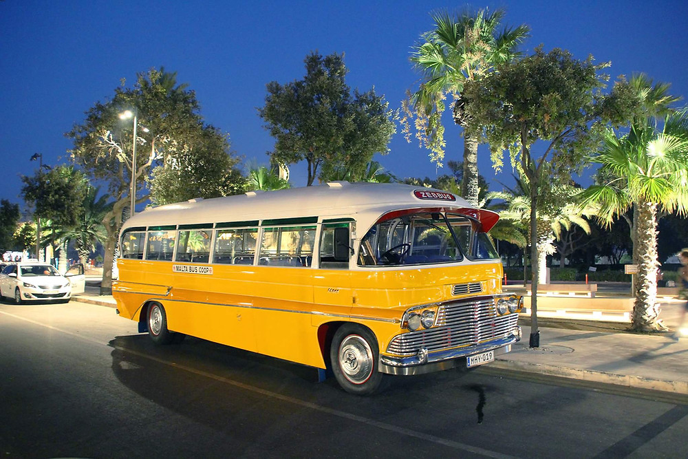 picture of old maltese bus bright yellow at night on a tree lined street