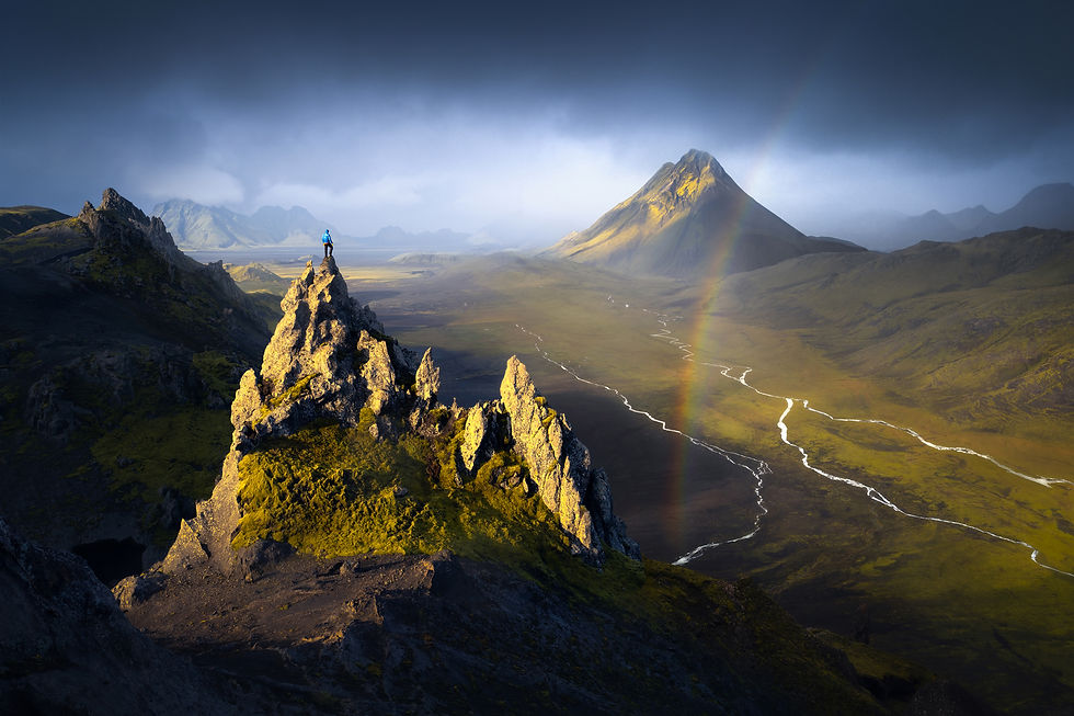 Hiker on rocky ridge with rainbow, volcanic mountain and glacial river in the Iceland Highlands