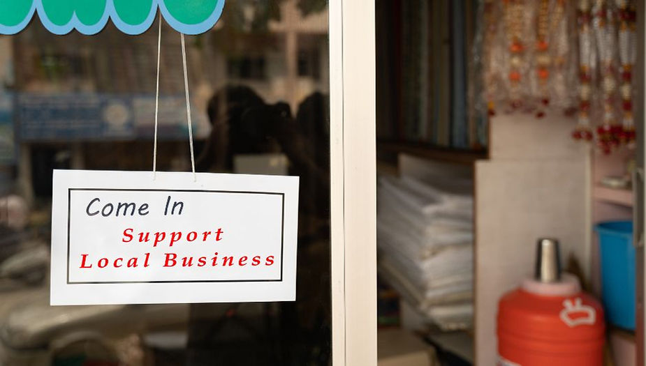 Sign reading 'Come In Support Local Business' on a storefront.